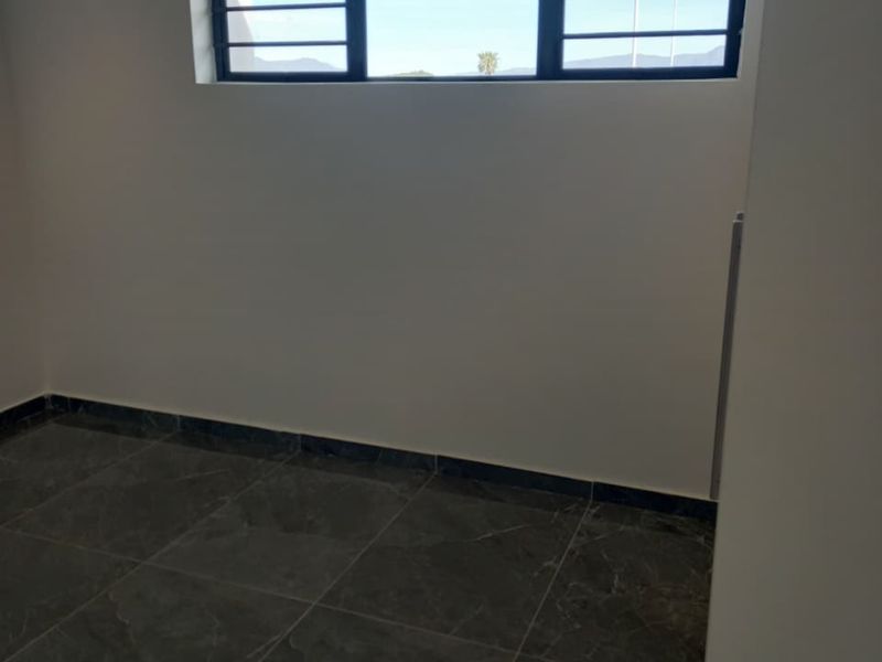 An empty bedroom featuring dark marble-look floor tiles and a window fitted with security bars.