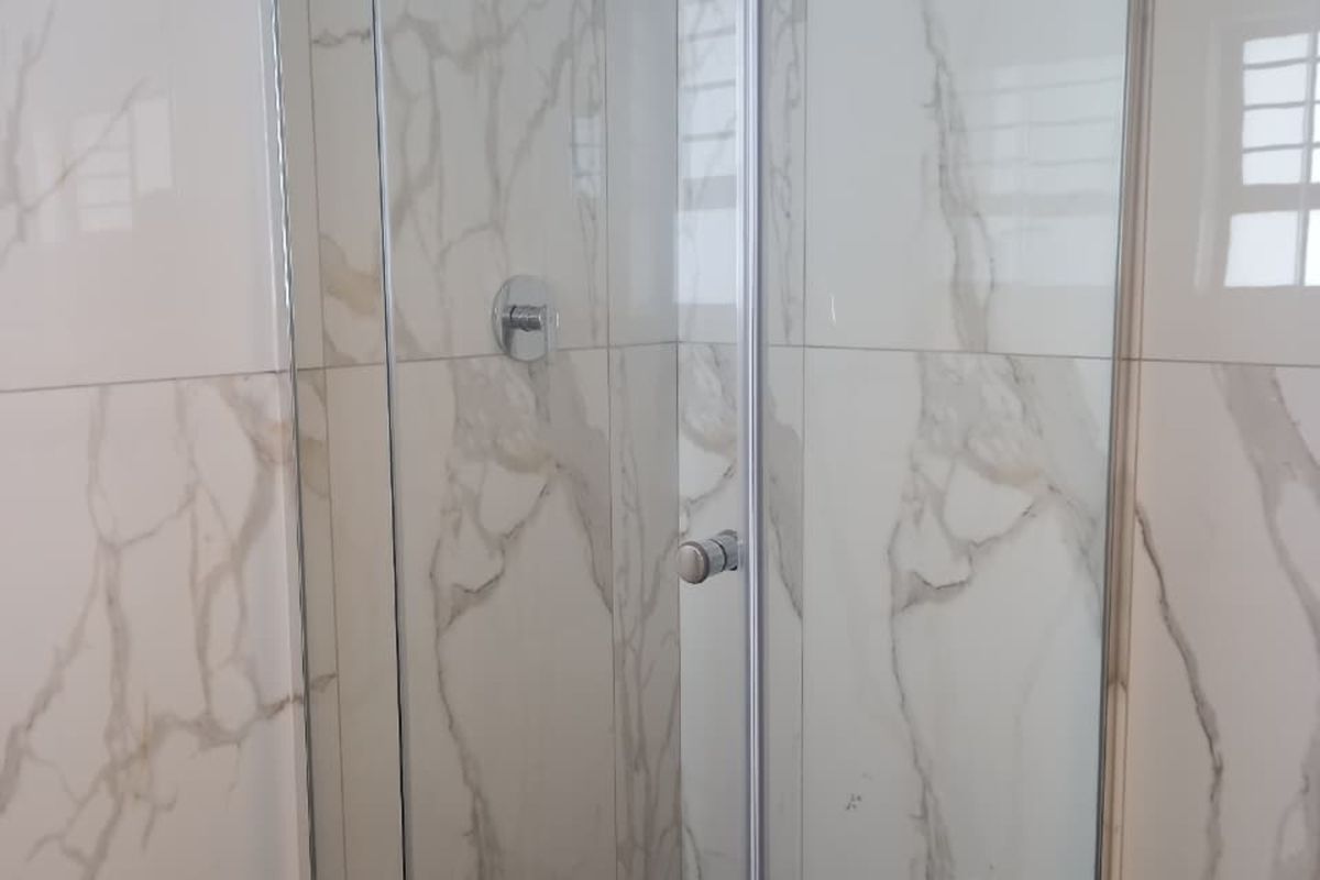 A modern bathroom shower featuring a glass enclosure, rainfall shower head, and elegant marble-look wall tiling.