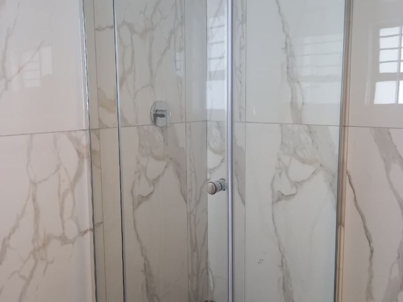 A modern bathroom shower featuring a glass enclosure, rainfall shower head, and elegant marble-look wall tiling.