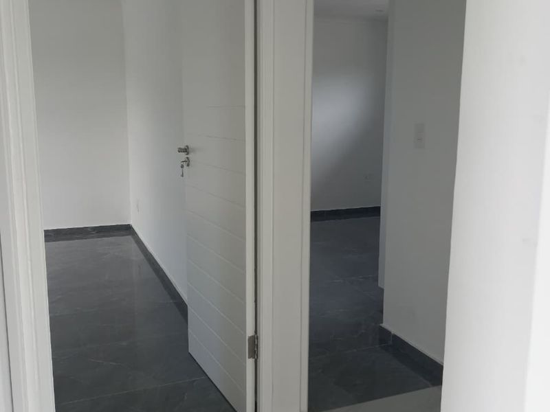 A bright, modern hallway featuring neutral white walls and dark grey tiled flooring, providing access to multiple rooms within the apartment.