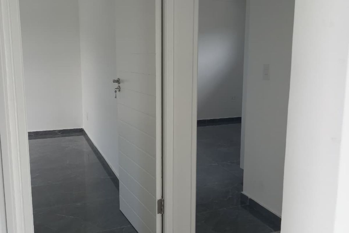 A bright, modern hallway featuring neutral white walls and dark grey tiled flooring, providing access to multiple rooms within the apartment.