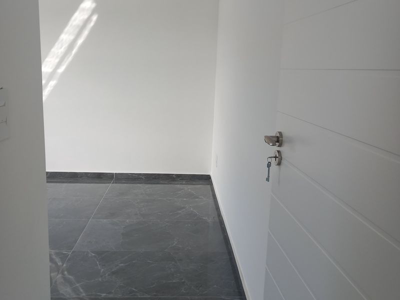 A bright, empty bedroom featuring modern dark marble-effect floor tiles, crisp white walls, and a clean, minimalist aesthetic.