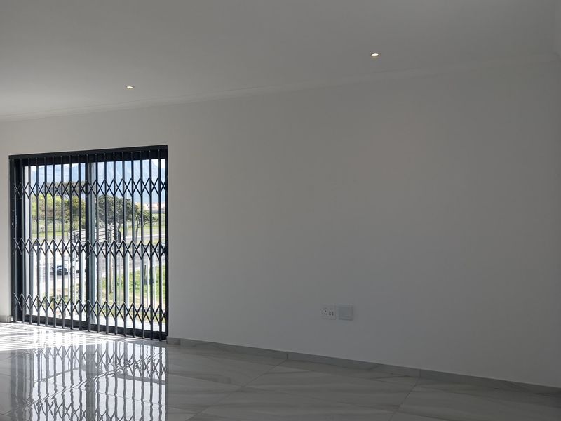 A bright, empty living area featuring modern porcelain tile flooring, recessed downlights, and a sliding glass door with a security gate.