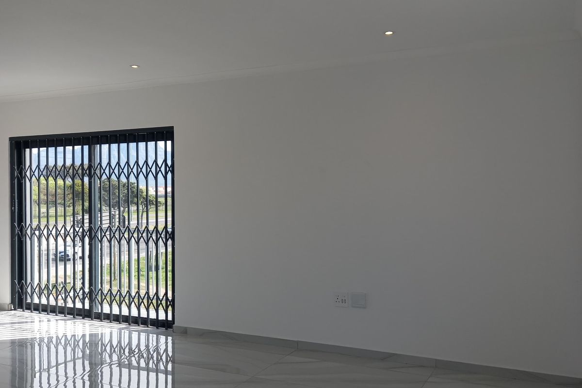 A bright, empty living area featuring modern porcelain tile flooring, recessed downlights, and a sliding glass door with a security gate.