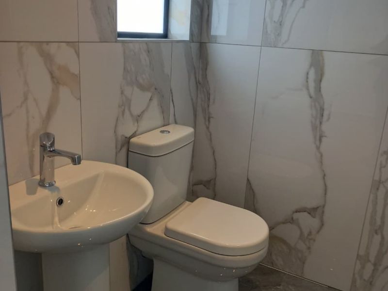 A modern, well-maintained bathroom featuring marble-look wall tiling, a pedestal basin with chrome fixtures, and a dual-flush toilet.