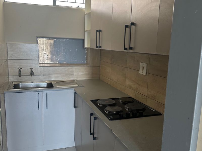 A compact, modern kitchen featuring neutral cabinetry, a built-in electric hob, stainless steel sink, and tiled finishes throughout.