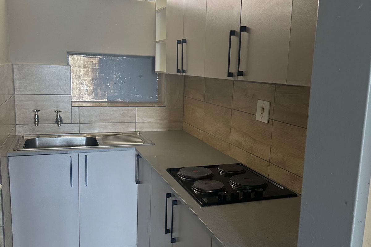 A compact, modern kitchen featuring neutral cabinetry, a built-in electric hob, stainless steel sink, and tiled finishes throughout.