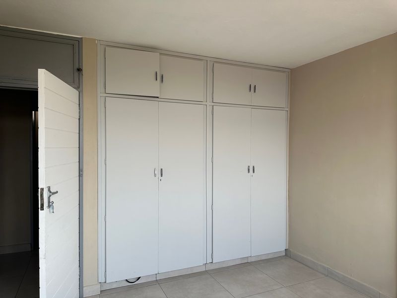 A clean, empty bedroom featuring neutral tiled flooring and ample built-in cupboard storage with overhead compartments.