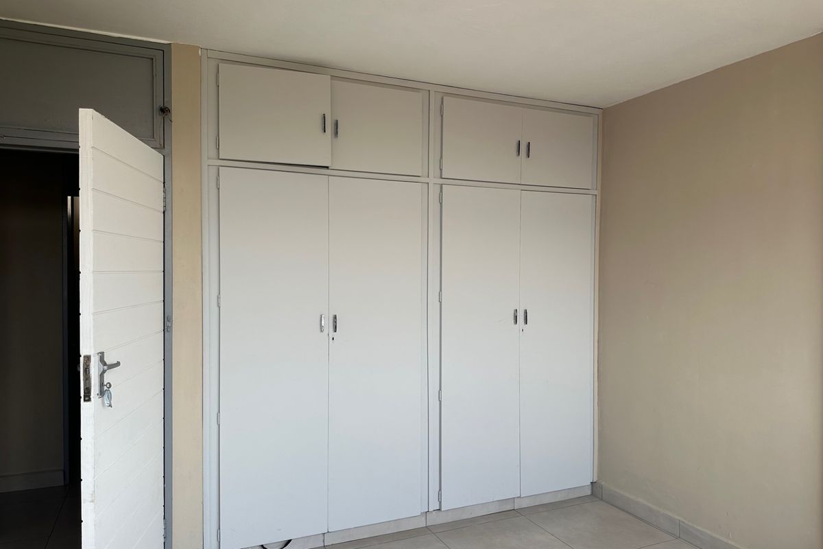 A clean, empty bedroom featuring neutral tiled flooring and ample built-in cupboard storage with overhead compartments.