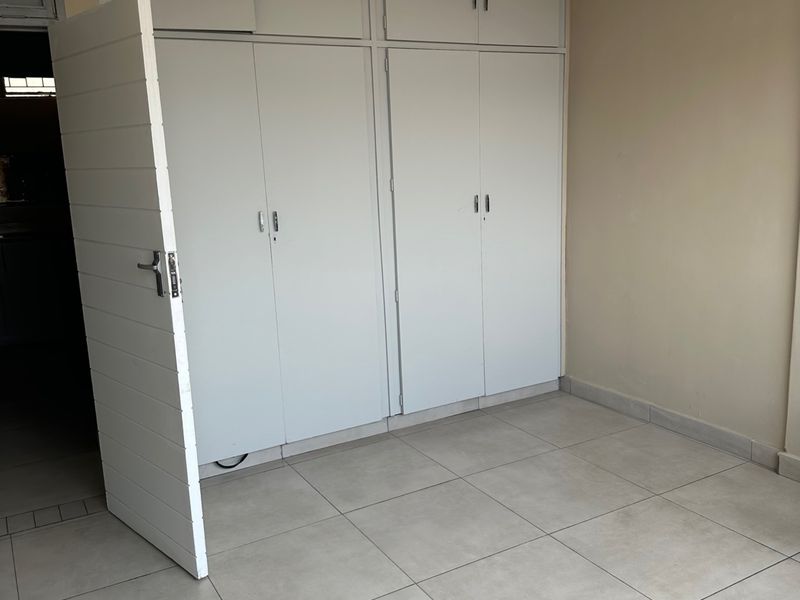 A clean, empty bedroom featuring neutral tiled flooring and extensive built-in cupboard storage with overhead cabinets.