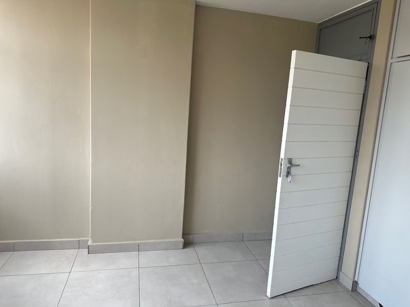 An empty bedroom featuring neutral wall paint, tiled flooring, and a built-in cupboard, offering a clean and versatile space ready for personalization.