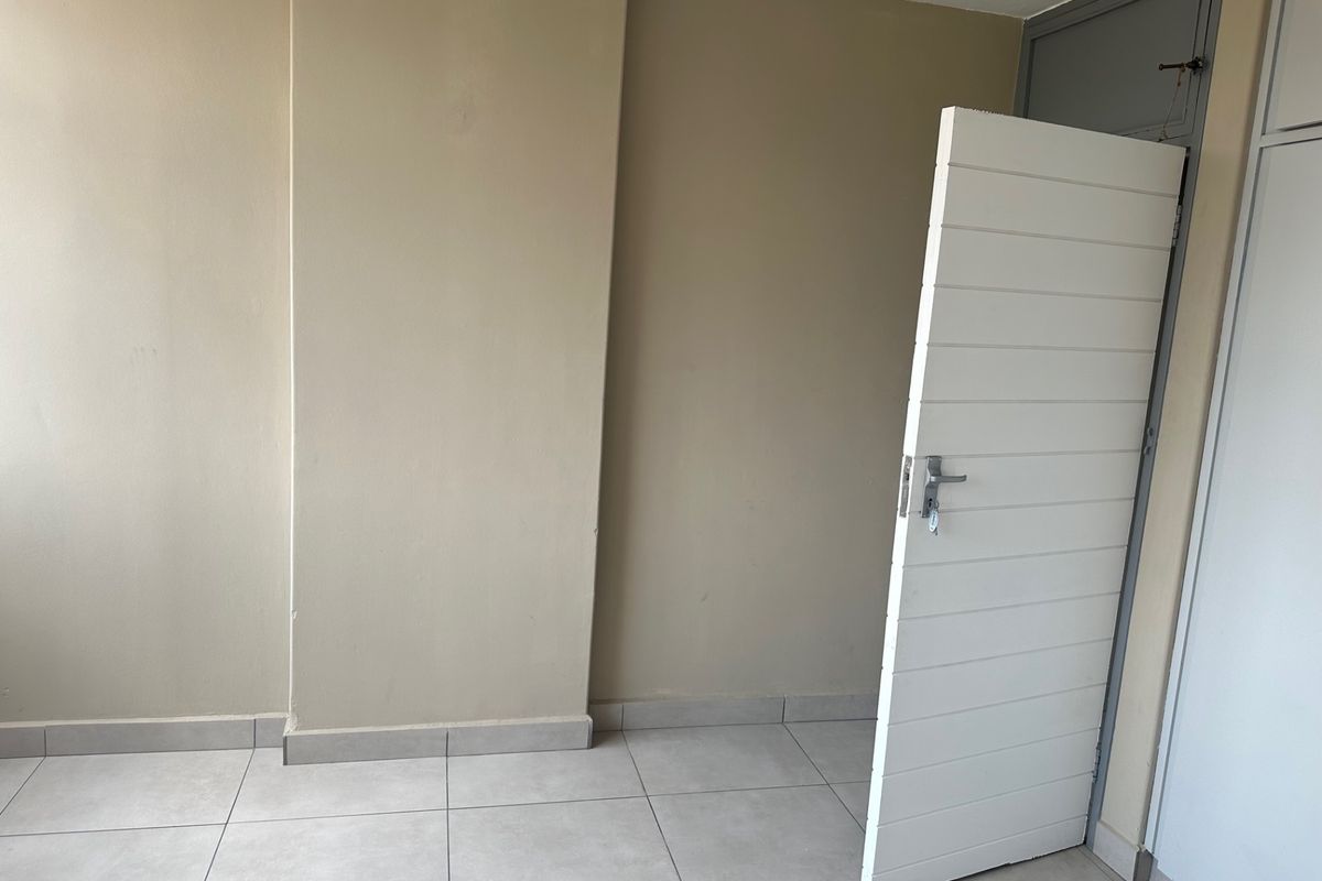 An empty bedroom featuring neutral wall paint, tiled flooring, and a built-in cupboard, offering a clean and versatile space ready for personalization.