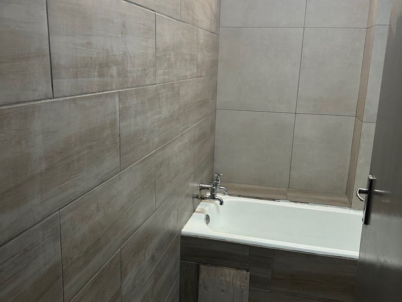 A functional bathroom featuring full-height wood-look wall tiling, a built-in bathtub with chrome fixtures, and a high-level window for natural light.