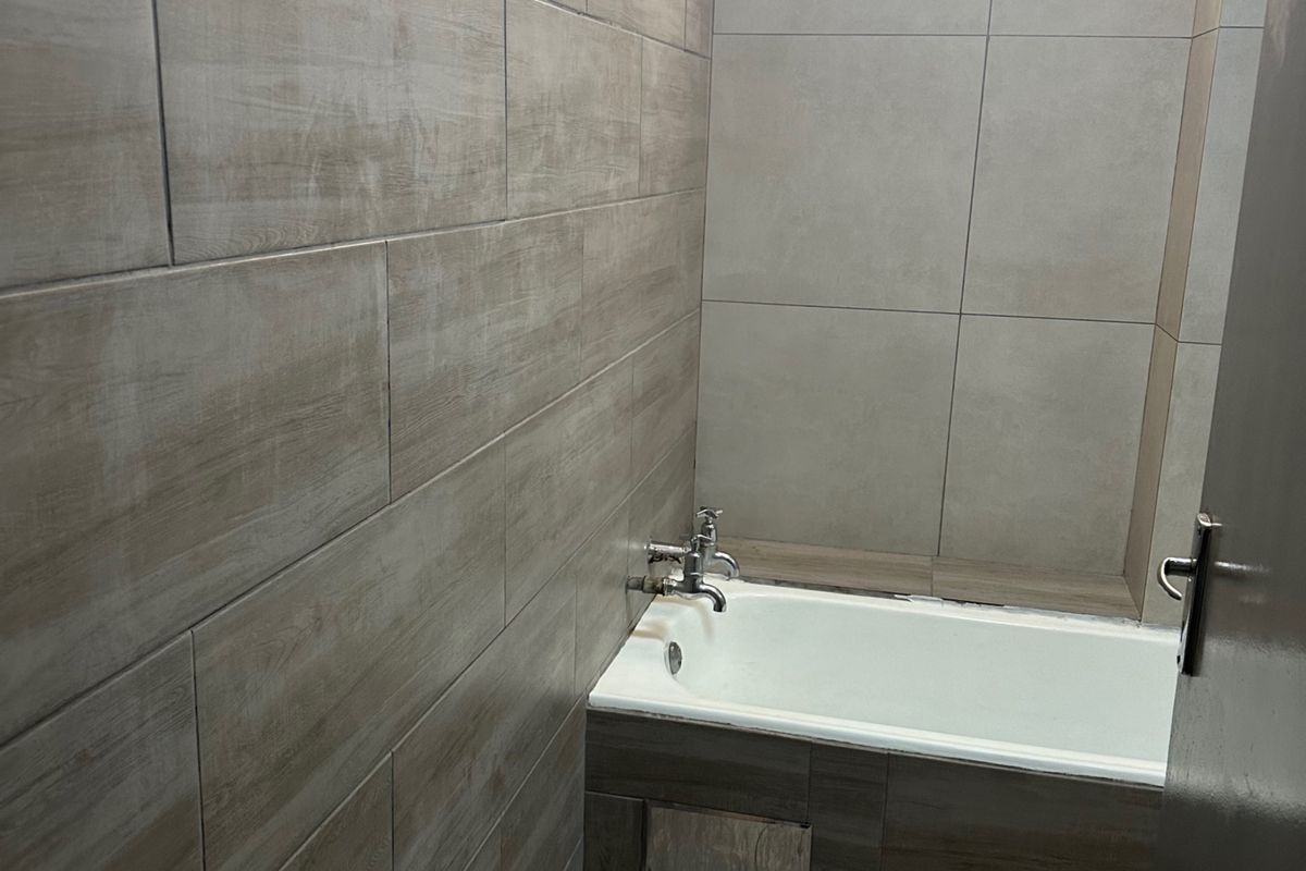 A functional bathroom featuring full-height wood-look wall tiling, a built-in bathtub with chrome fixtures, and a high-level window for natural light.