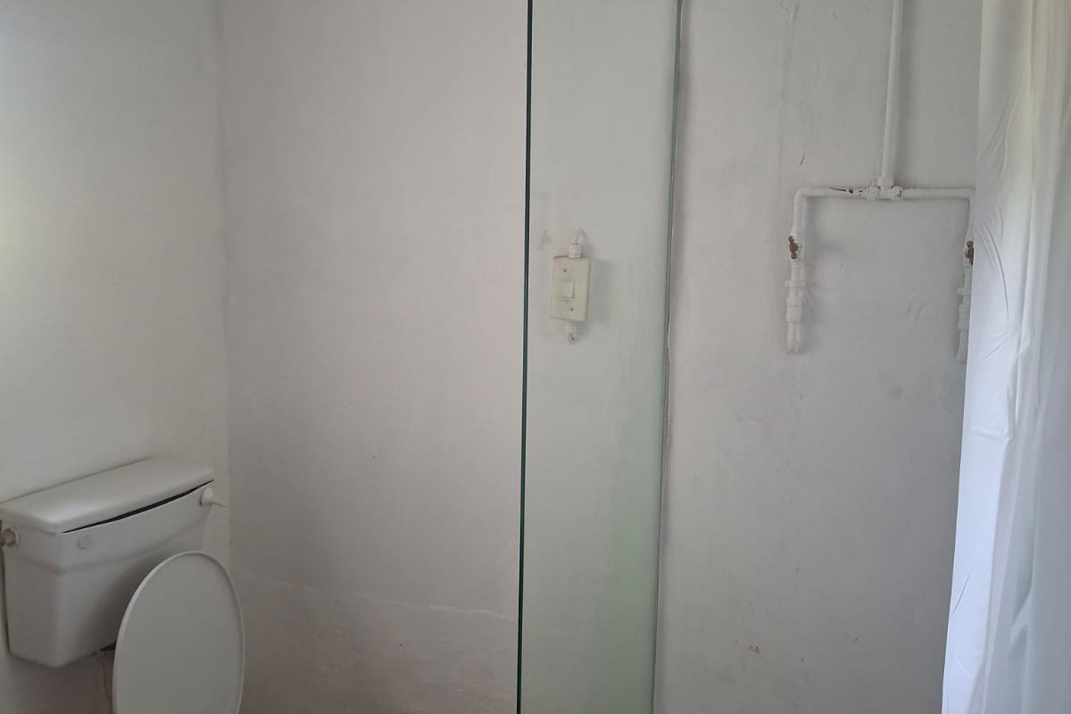 A functional bathroom featuring a toilet and a walk-in shower area with a glass partition and exposed plumbing fixtures.