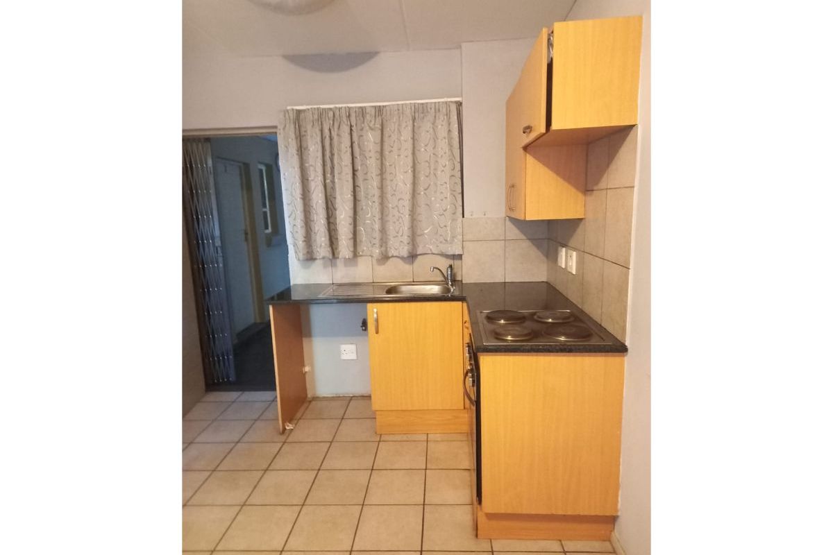 Compact kitchen featuring laminate cabinetry, built-in oven, electric hob, and tiled flooring. The space requires minor repairs to cabinetry.