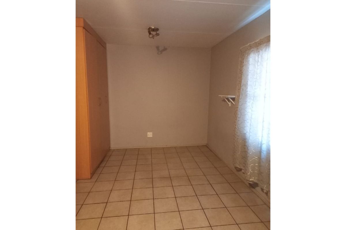 A vacant bedroom featuring neutral tiled flooring, a built-in wardrobe, and a window with existing curtain hardware.
