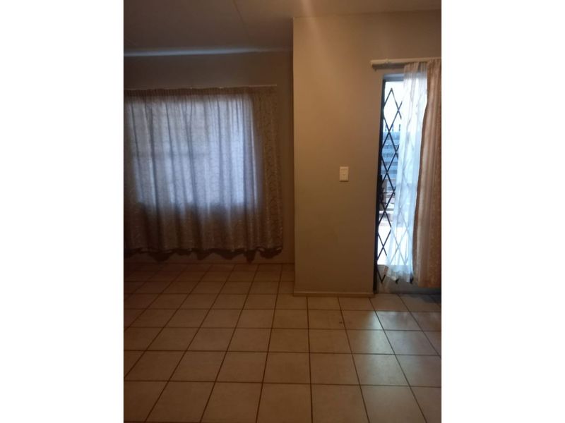An empty living area featuring neutral ceramic floor tiles, a security gate at the entrance, and installed curtain rails.