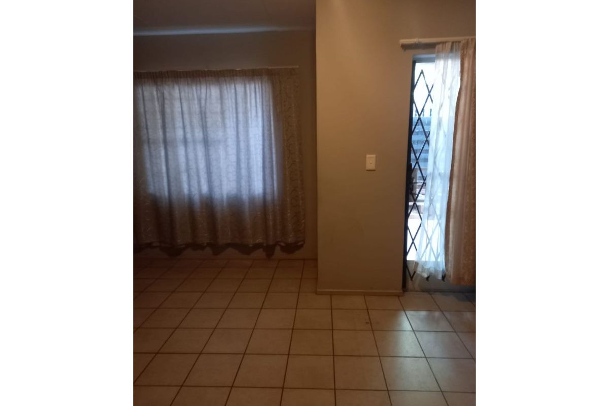 An empty living area featuring neutral ceramic floor tiles, a security gate at the entrance, and installed curtain rails.
