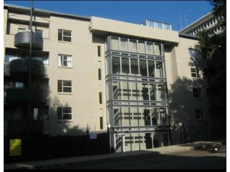 Front elevation of a multi-story apartment building featuring a prominent glass facade, curved balconies, and secure perimeter fencing.