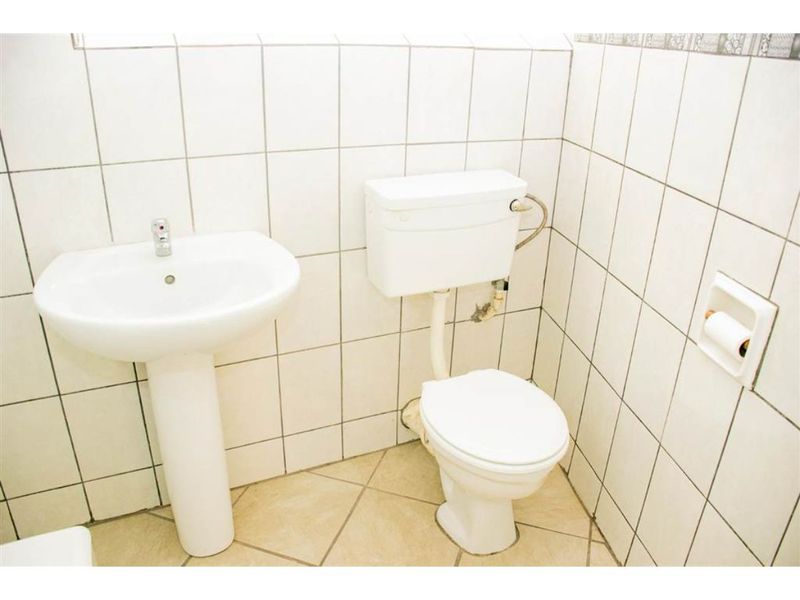 A functional bathroom featuring a white pedestal basin, standard toilet, and full-height ceramic wall tiling.
