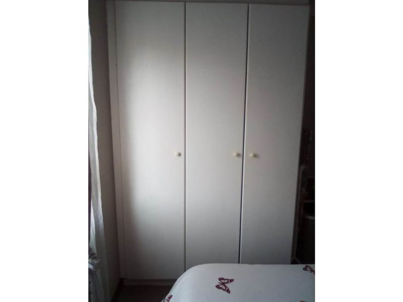 A bedroom featuring a white built-in wardrobe with three doors.