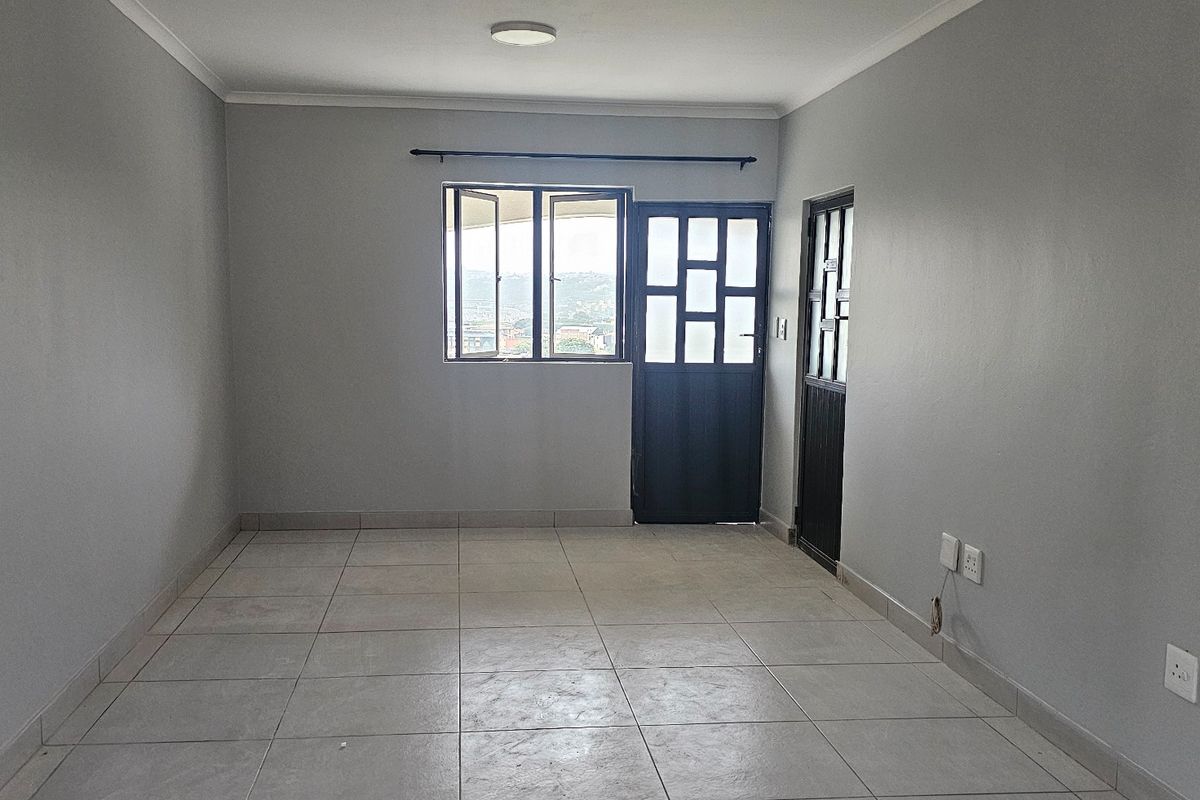 An empty living room featuring neutral grey walls, tiled flooring, and direct access to an exterior area through a dark-framed door.