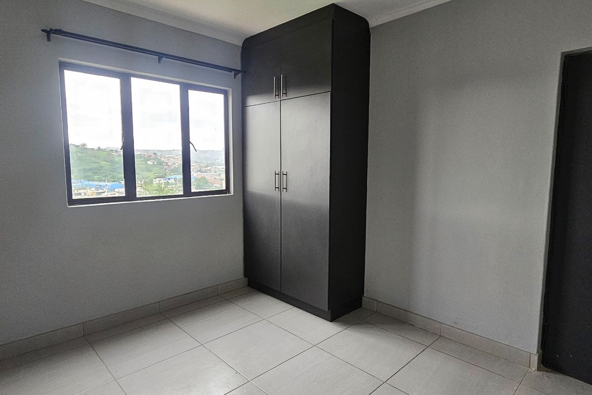 A clean, empty bedroom featuring neutral wall paint, tiled flooring, and a dark built-in wardrobe with ample storage space.