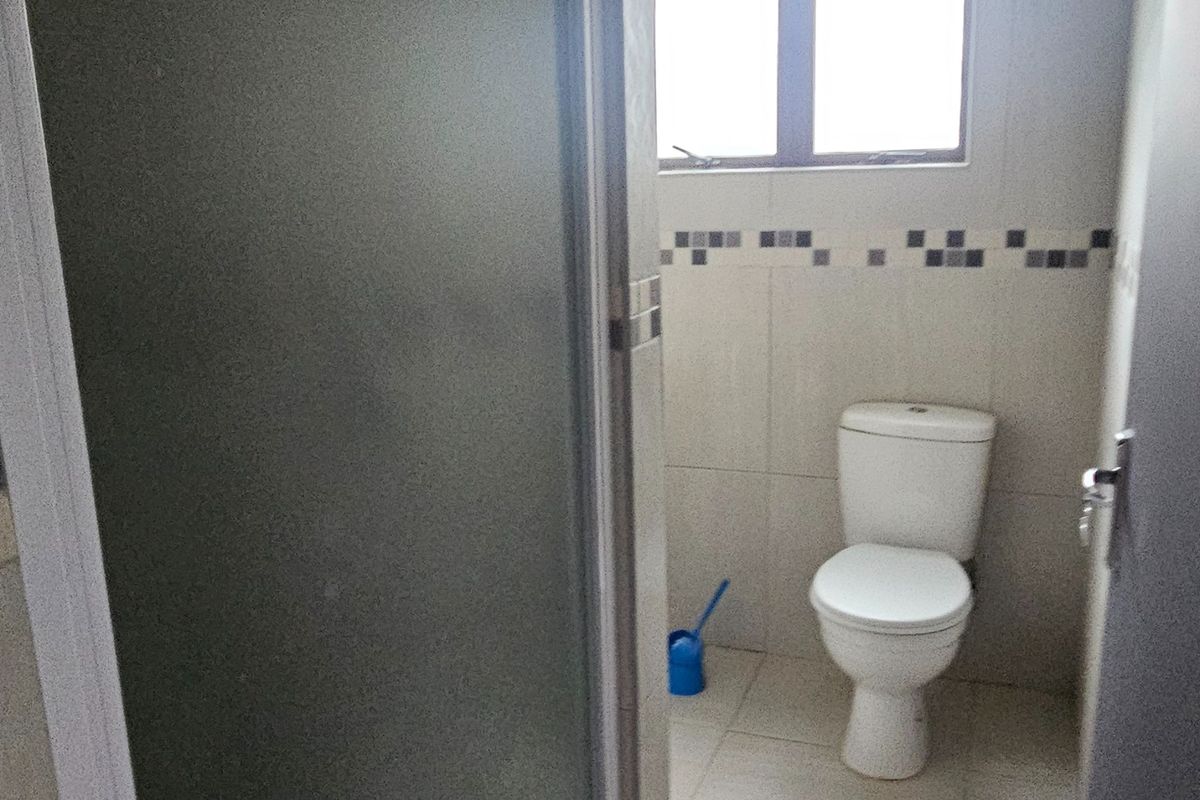 A functional bathroom featuring a shower enclosure, toilet, and neutral tiled finishes throughout.
