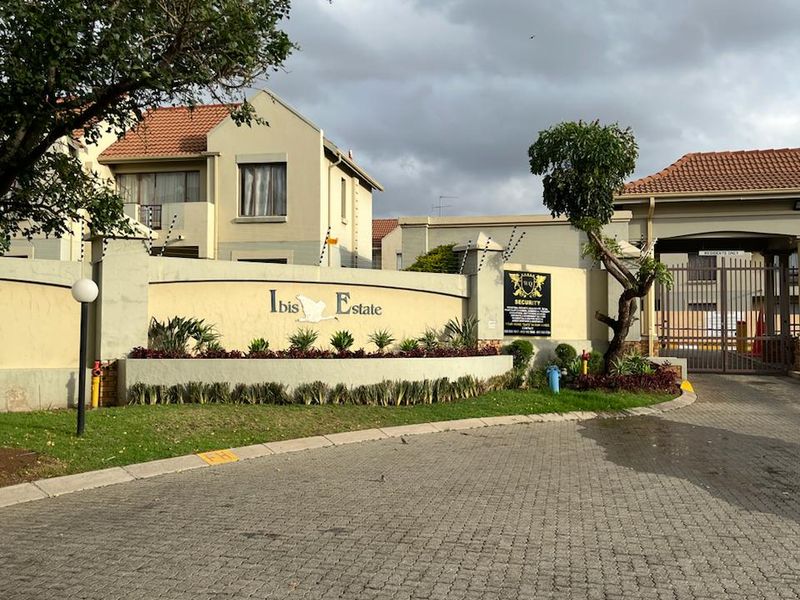 Front entrance view of Ibis Estate featuring a paved driveway, secure gated access, perimeter wall with electric fencing, and established garden landscaping.