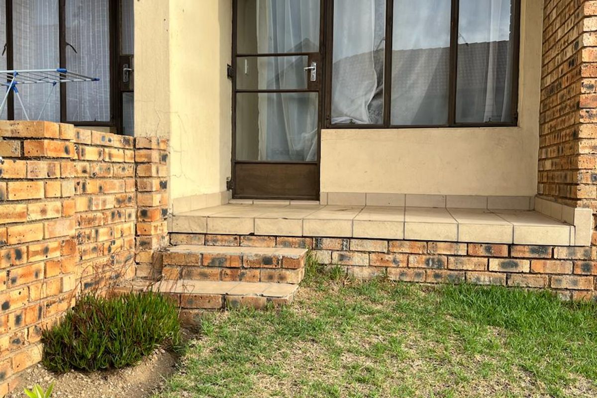 A ground-level patio area featuring brick retaining walls, tiled flooring, and direct access to the interior through a security screen door.