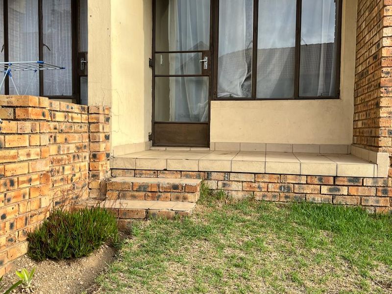 A ground-level patio area featuring brick retaining walls, tiled flooring, and direct access to the interior through a security screen door.