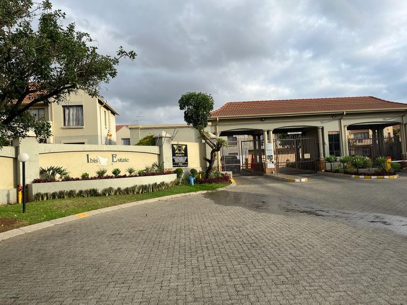 The entrance to Ibis Estate featuring a paved driveway, secure gated access, and perimeter walling with electric fencing.
