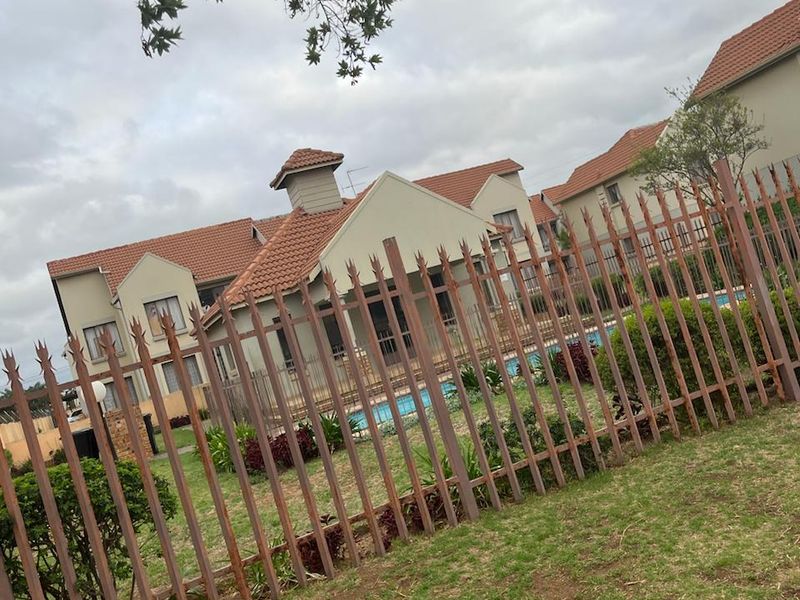 View of the rear exterior of the property featuring a swimming pool, landscaped garden, and secure metal spike fencing.