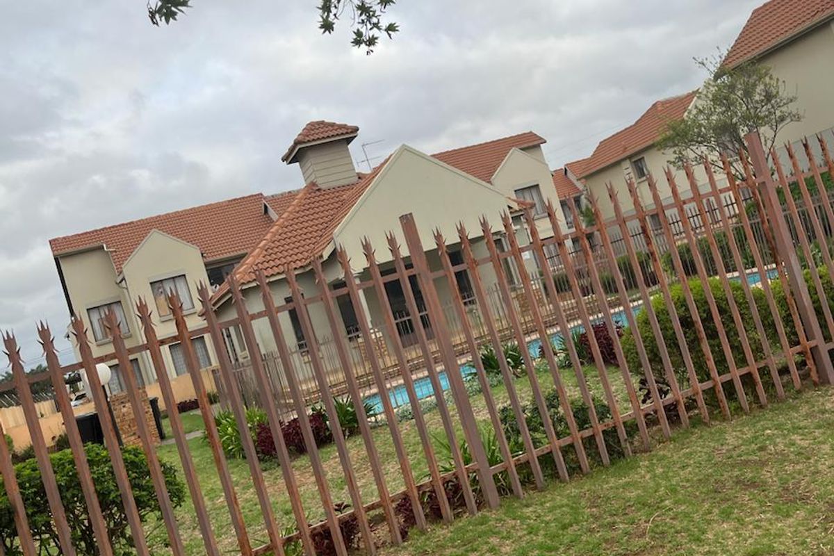 View of the rear exterior of the property featuring a swimming pool, landscaped garden, and secure metal spike fencing.