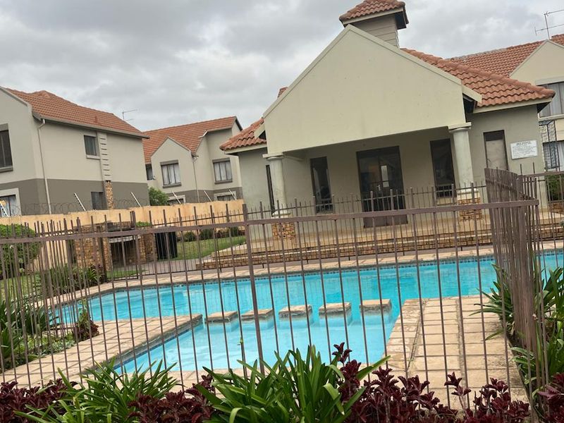 Communal pool area featuring a paved surround, metal safety fencing, and a built-in braai facility within a well-maintained residential complex.