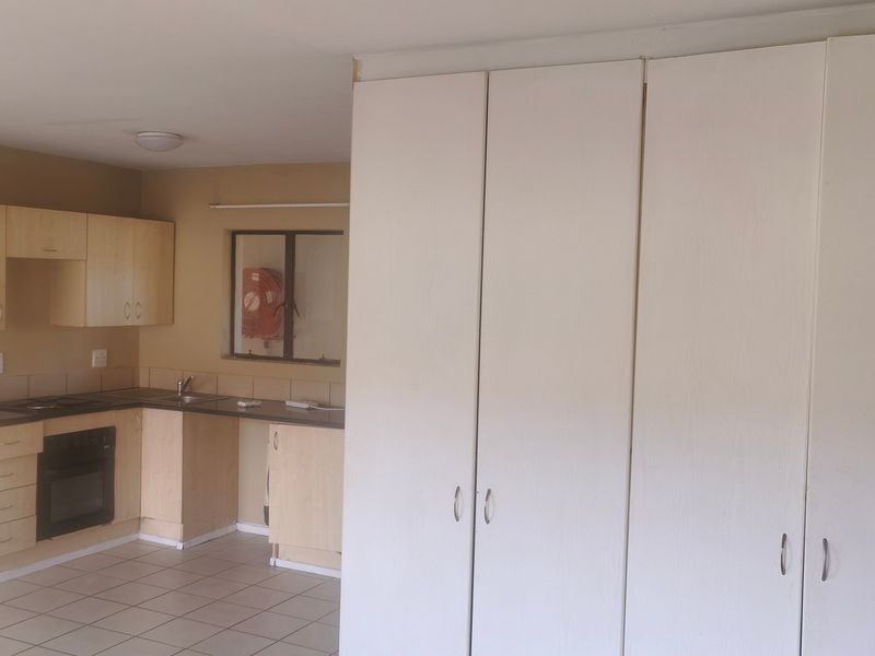 Open plan kitchen area featuring light wood cabinetry, built-in oven and hob, and tiled flooring, adjacent to a large wall of built-in storage cupboards.