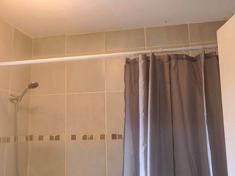 A functional bathroom shower area featuring wall tiling and a standard shower head, currently showing signs of wear on the ceiling and grout.