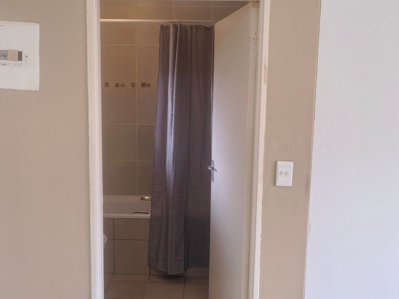 A view into a functional bathroom featuring a bathtub with tiled surrounds and neutral wall finishes, adjacent to an electrical distribution board.