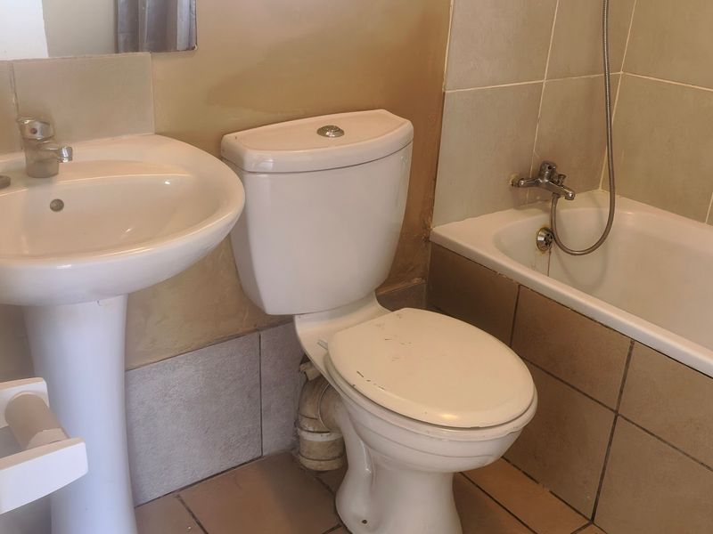 A functional bathroom featuring a pedestal basin, toilet, and bathtub with shower mixer, finished with tiled walls and flooring in need of cosmetic updates.