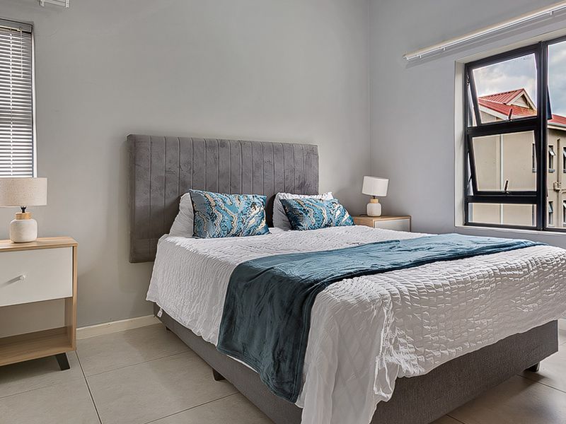 A well-maintained bedroom featuring neutral wall tones, tiled flooring, and large aluminium-framed windows that provide ample natural light.