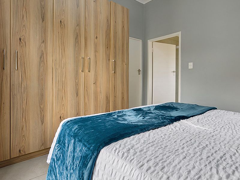 A well-maintained bedroom featuring modern wood-finish built-in cupboards and neutral tiled flooring.