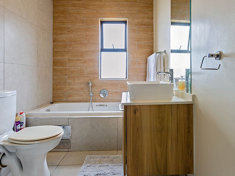 Modern bathroom featuring a built-in bathtub, wood-finish vanity with a vessel sink, and neutral wall tiling.