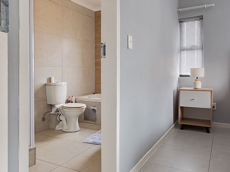 A bedroom featuring tiled flooring and a direct view into an en-suite bathroom equipped with a toilet and bathtub.