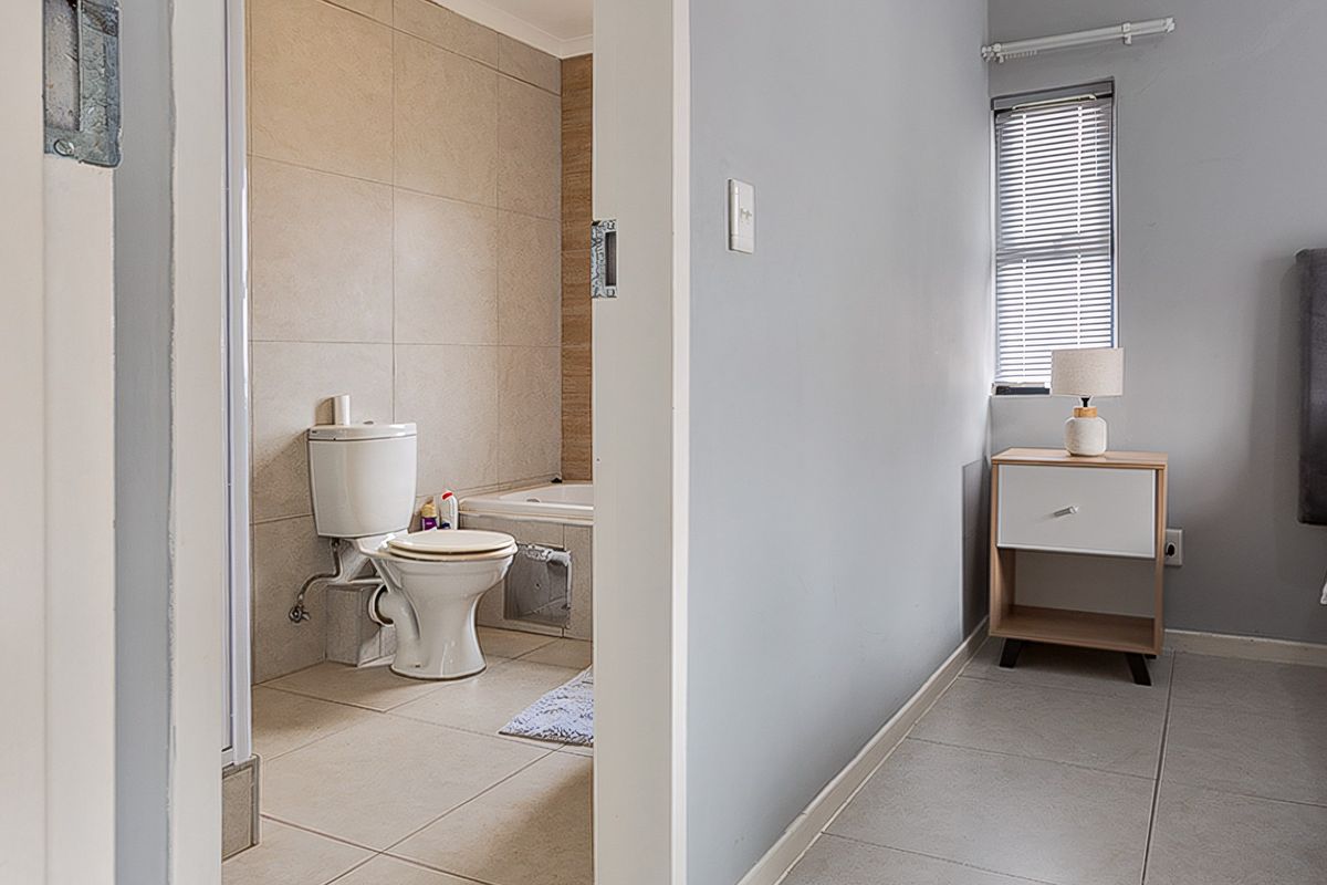 A bedroom featuring tiled flooring and a direct view into an en-suite bathroom equipped with a toilet and bathtub.
