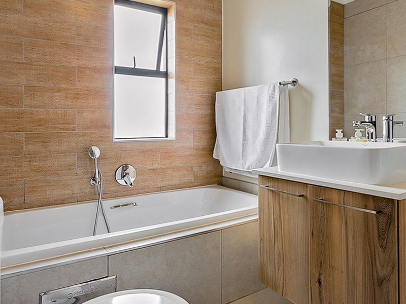 Modern bathroom featuring a built-in bathtub, wood-finish vanity with a vessel sink, and stylish tiled feature wall.