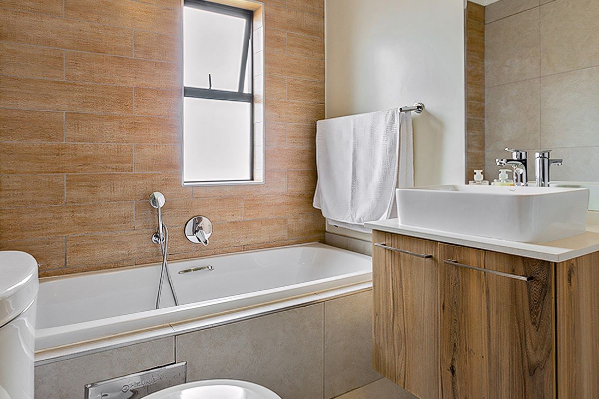 Modern bathroom featuring a built-in bathtub, wood-finish vanity with a vessel sink, and stylish tiled feature wall.