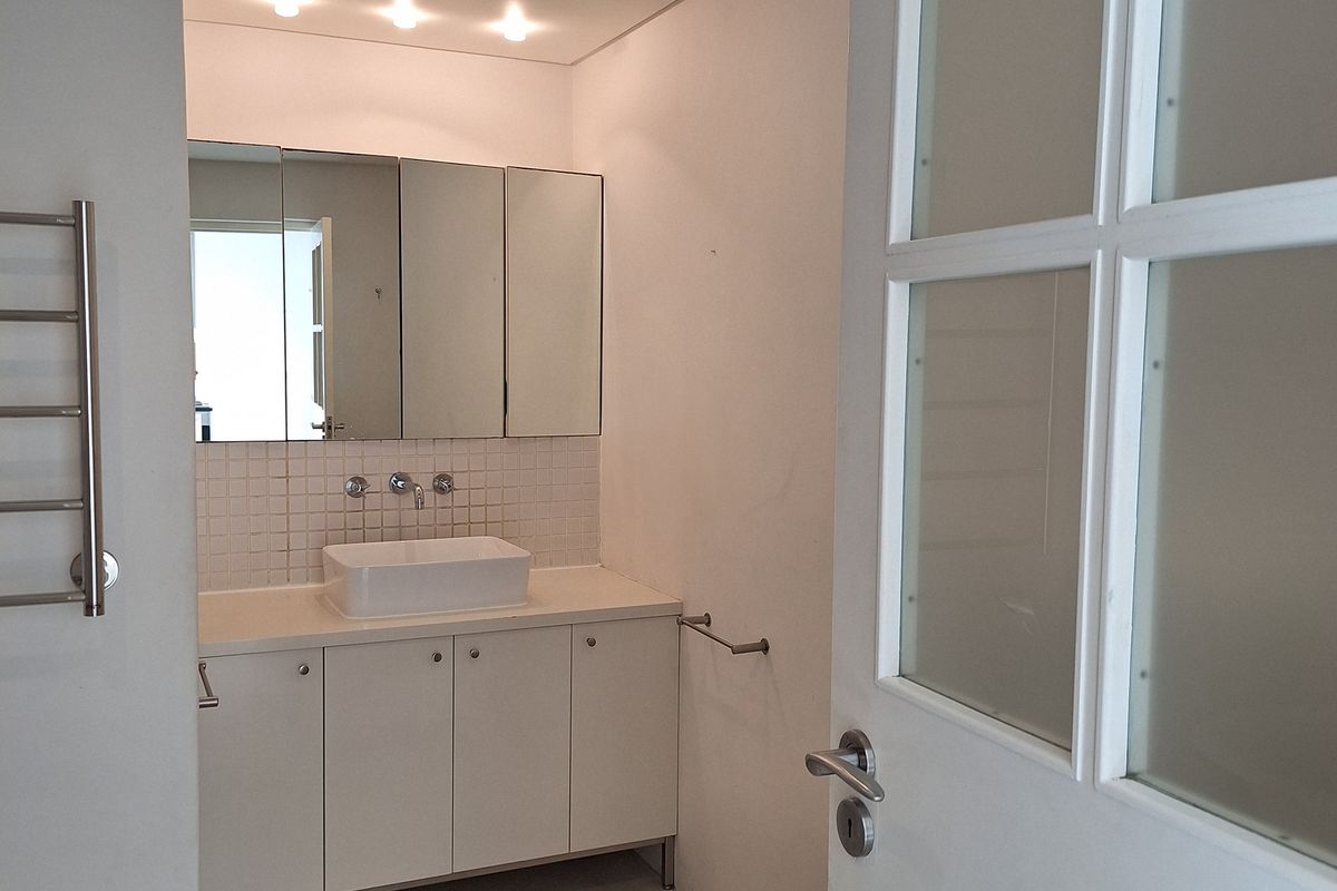 A modern bathroom featuring a vessel sink on a white vanity, mirrored medicine cabinet, heated towel rail, and recessed lighting.