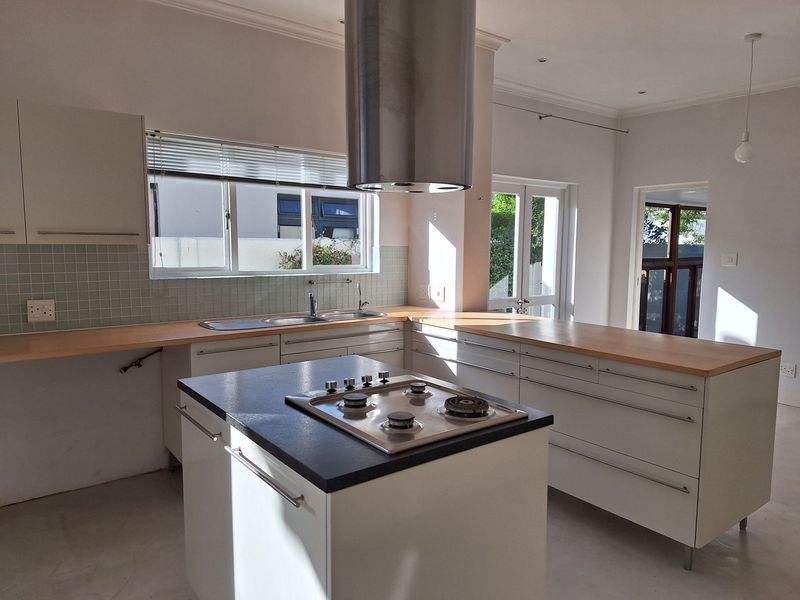 A bright, modern kitchen featuring a central island with a gas hob, stainless steel extractor, wooden countertops, and ample built-in cabinetry.