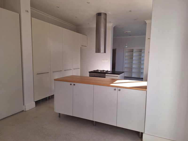 A modern, minimalist kitchen featuring white cabinetry, a central island with a wooden countertop, and a stainless steel extractor fan.